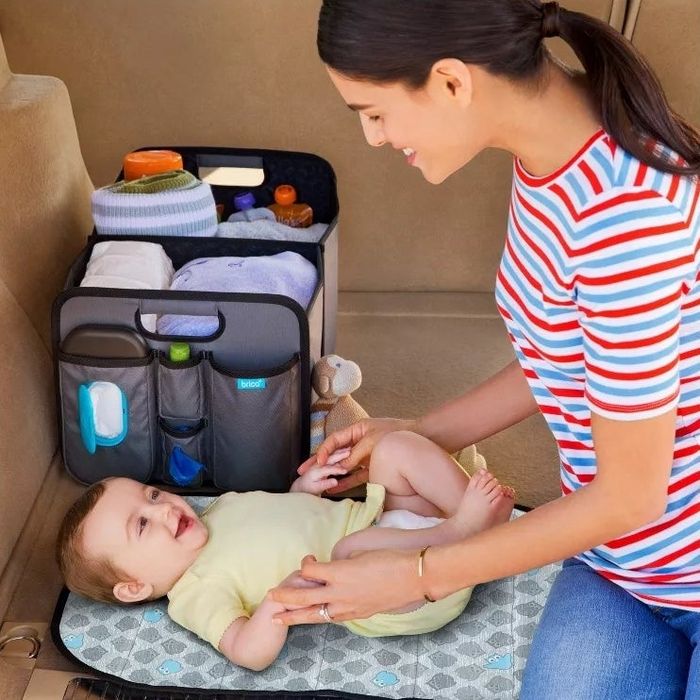 Person changing a baby on a portable changing pad, with a car organizer full of supplies nearby