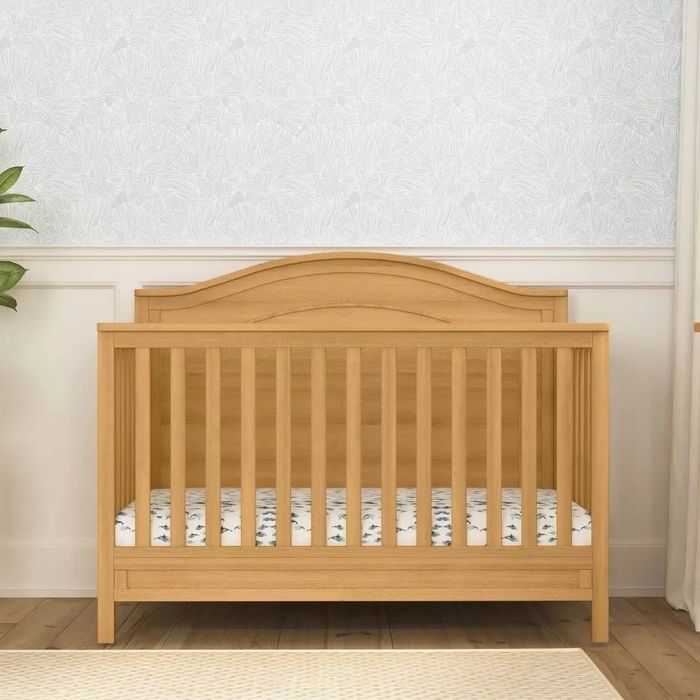 Wooden crib set against a patterned wall, without bedding, for an article on nursery furniture shopping.