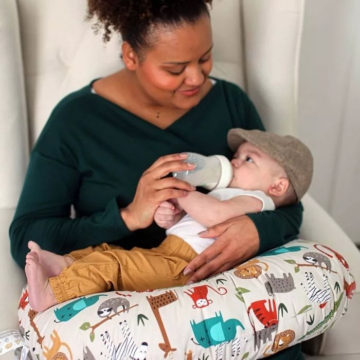 A model feeding a baby with a bottle, sitting comfortably with a nursing pillow featuring an animal print design.