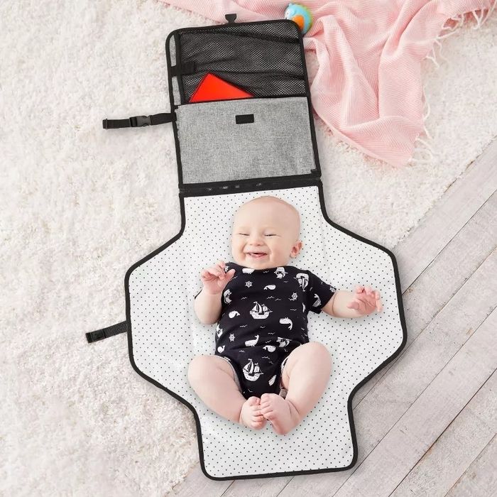 A baby lies joyfully on a diaper bag that has a built-in changing pad, looking content and happy.