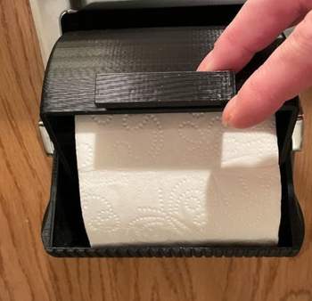 A toilet paper roll encased in a black protector that stops pets from unraveling it.