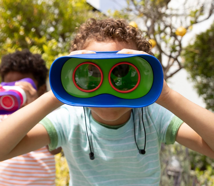 Two children using toy binoculars outdoors, eagerly searching the horizon