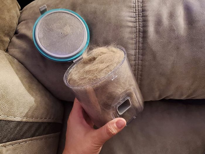 A hand holding the vacuum canister filled with cat fur