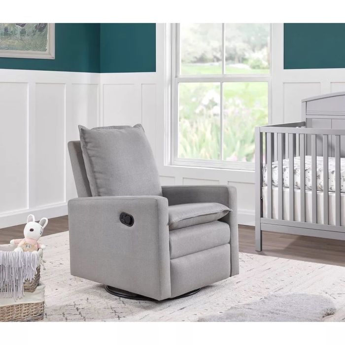 A gray nursery swivel glider reclining chair placed beside a crib.