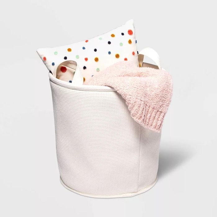 A textured laundry basket with towels and a cute polka dot cushion poking out from inside.