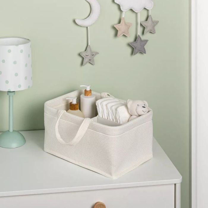 A woven diaper caddy, neatly arranged with baby essentials, placed on a dresser beside a soft lamp.