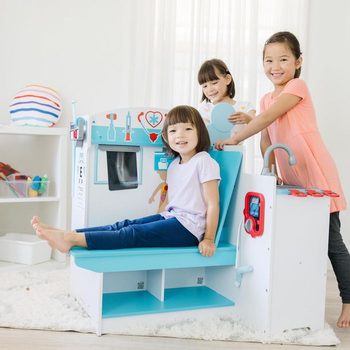 Three children happily play with a pretend doctor's office set, fully engaged with toy instruments and accessories