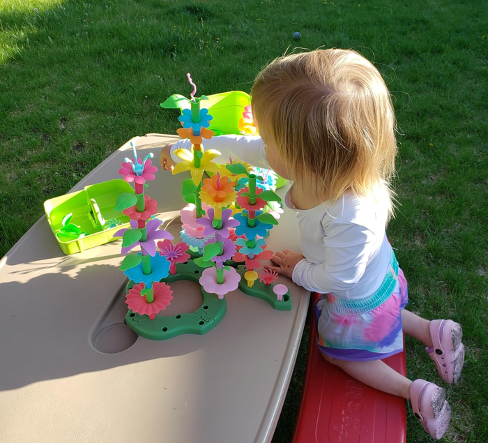A toddler enjoying a colorful flower and butterfly stacking toy on an outdoor plastic play table