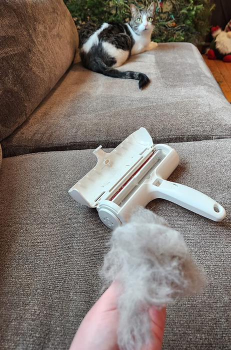 A reviewer proudly displaying all the fur the ChomChom collected from their couch, with their cat lounging in the background.