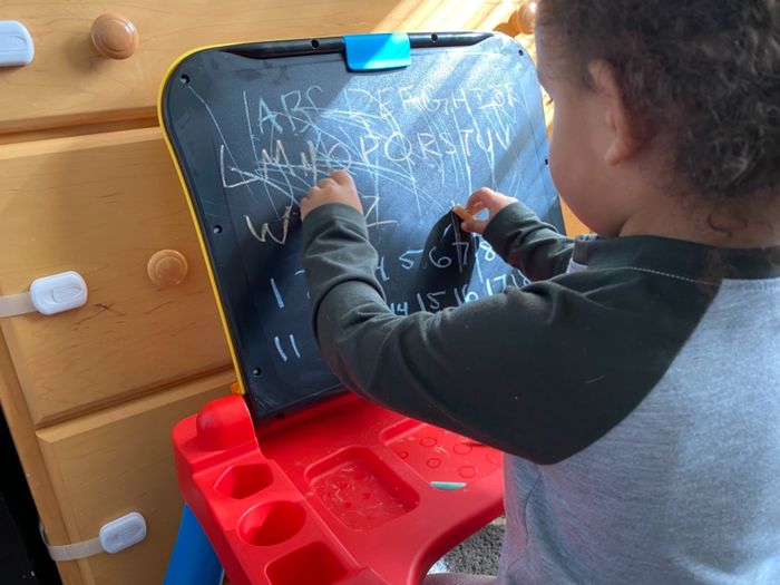 A child drawing on a small blackboard with chalk, standing on a chair