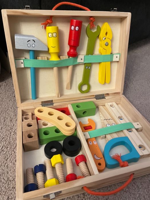 A brightly colored wooden toy tool kit with a hammer, wrench, pliers, screws, and bolts