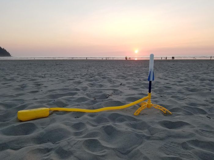 A toy rocket launcher set placed on a sandy beach as the sun sets in the background