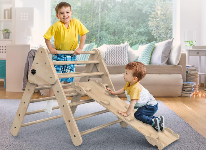Two children enjoy climbing on wooden climbing furniture, working their way across the bars