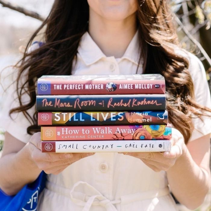 A model holding five books: The Perfect Mother, The Mans Room, Still Lives, How To Walk Away, and Small Country.