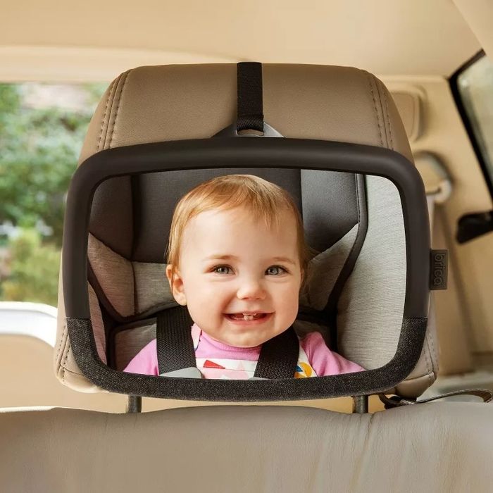 A toddler smiling happily in a secure car seat, with the headrest adjusted for comfort and safety.