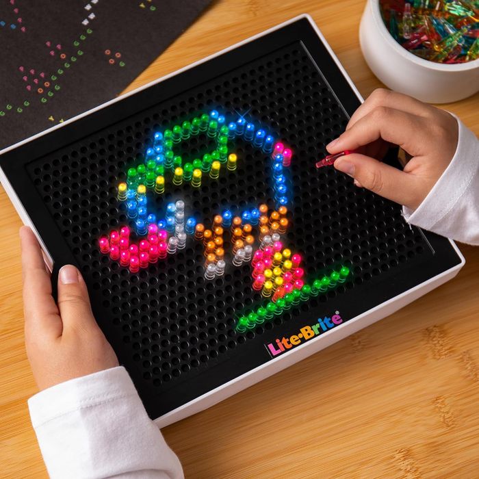 Hands arranging colorful pegs to create a parrot design on a Lite-Brite board