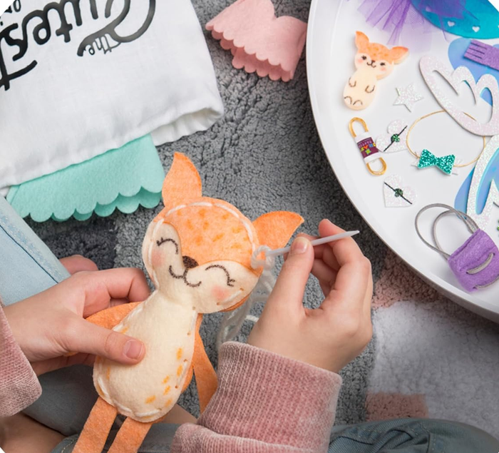 A person sewing a plush fox toy, featuring orange and white fabric, surrounded by craft supplies