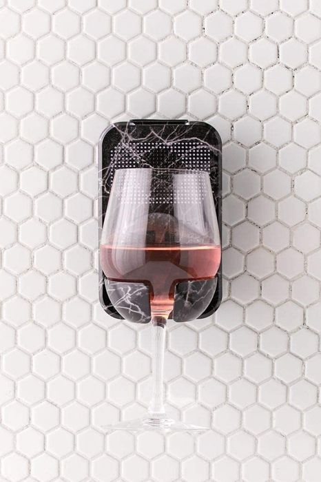 The black marble print caddy holding a wine glass against a tile wall