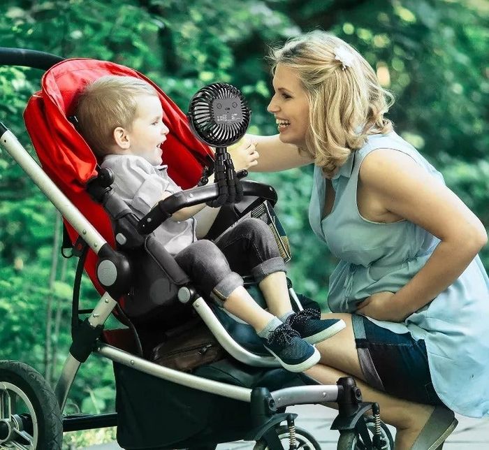 model smiling at a child in a stroller with a clip-on fan attached