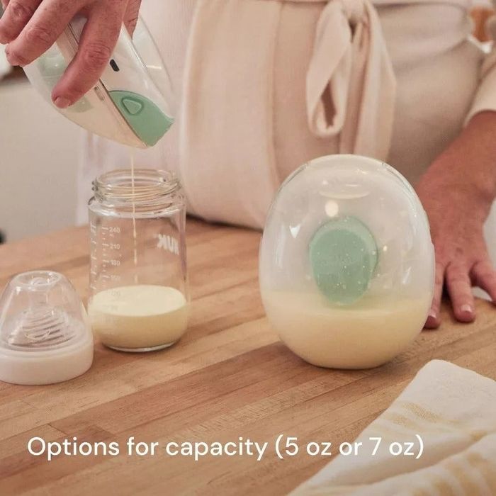 Person pouring milk from the pumps into a clear, egg-shaped baby bottle, displaying capacity options