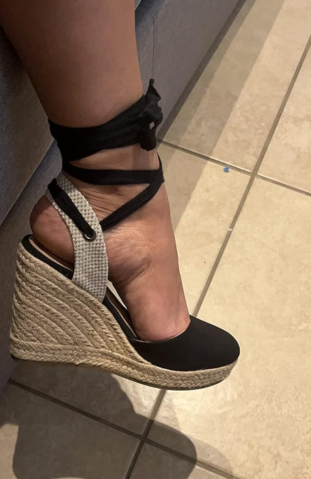 A person trying on a black-tie ankle strap wedge shoe
