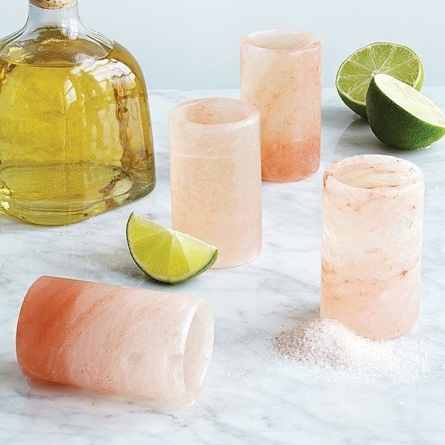 Four pink shot glasses placed next to limes and tequila.