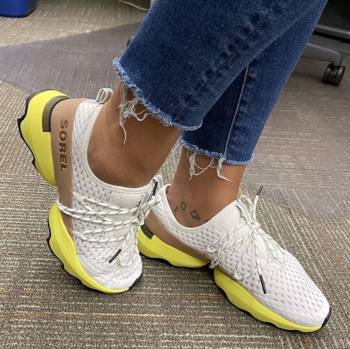 A reviewer wearing white sneakers with a yellow sole