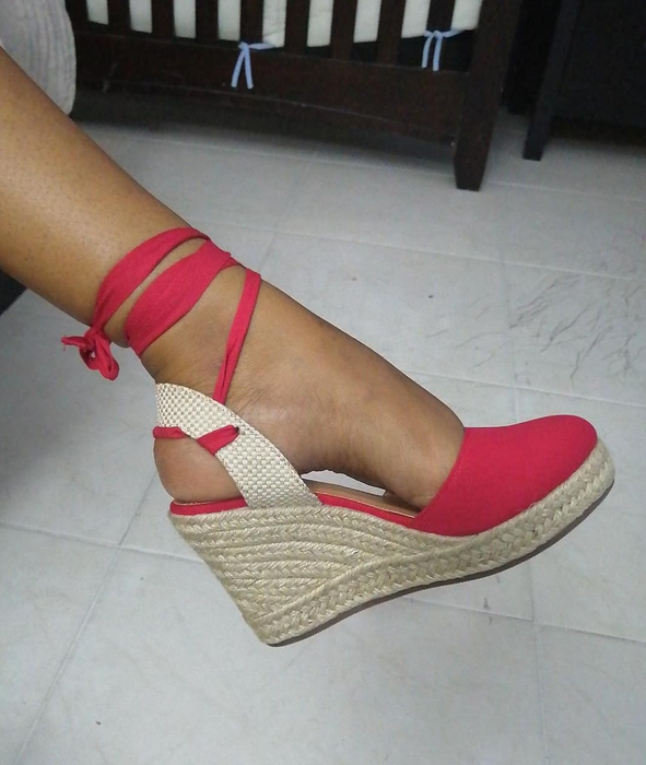 A person wearing a red wedge espadrille shoe with ankle ties