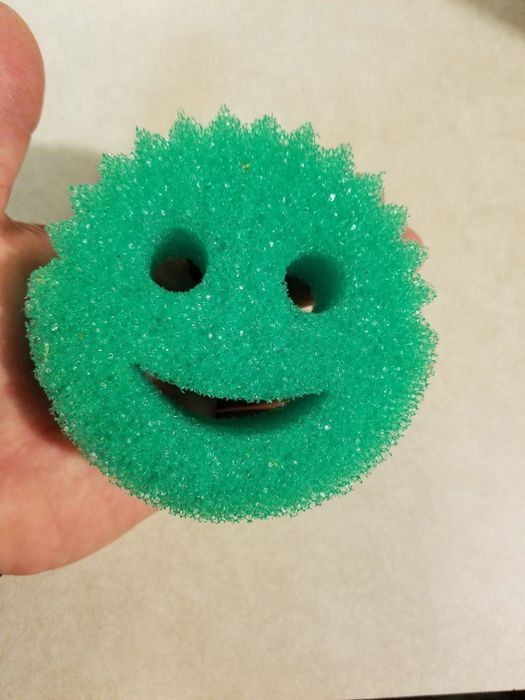 A reviewer holding the green smiley-faced sponge in their hand