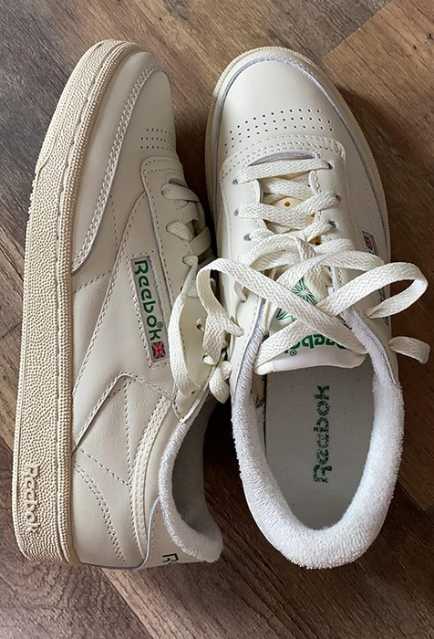 A close-up of two Reebok sneakers on a wooden floor, highlighting their design and logo.