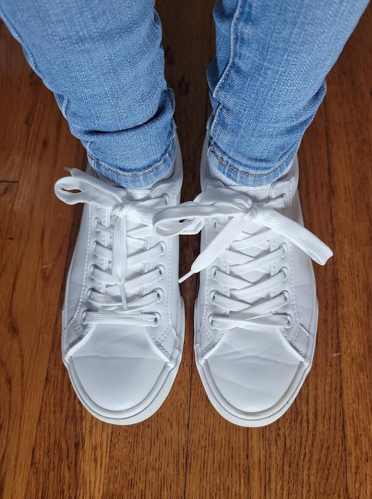 A person in white sneakers and blue jeans, standing on a wooden floor