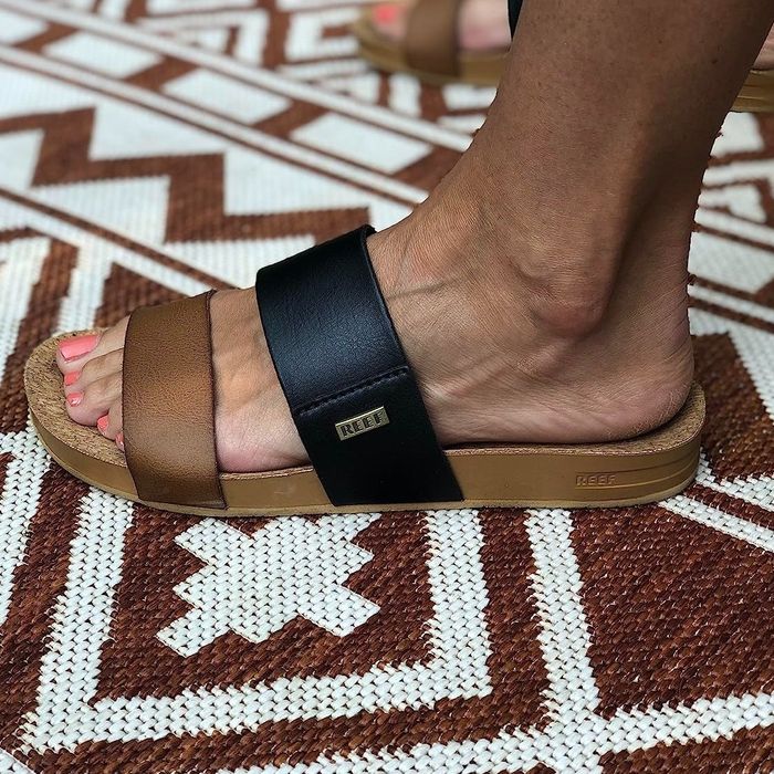 A close-up of a reviewer's feet in two-toned sandals