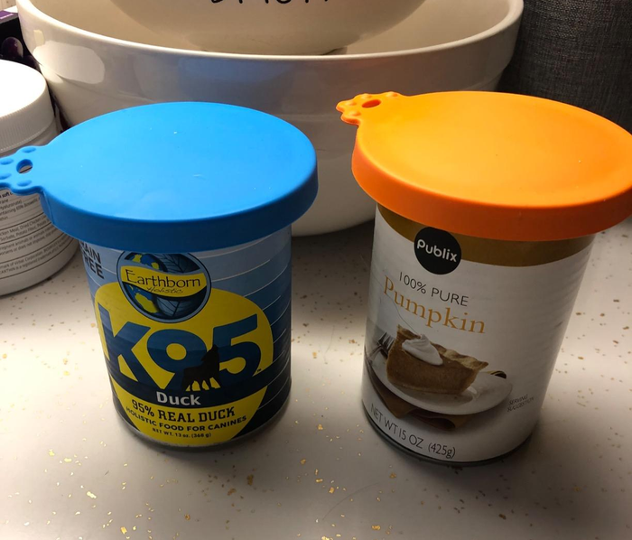 A reviewer showing their blue and orange silicone lids placed on top of cans of dog food.