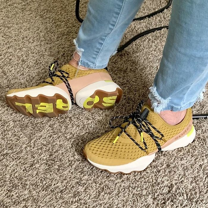 A reviewer wearing tan sneakers, showing that the sole bottom reads