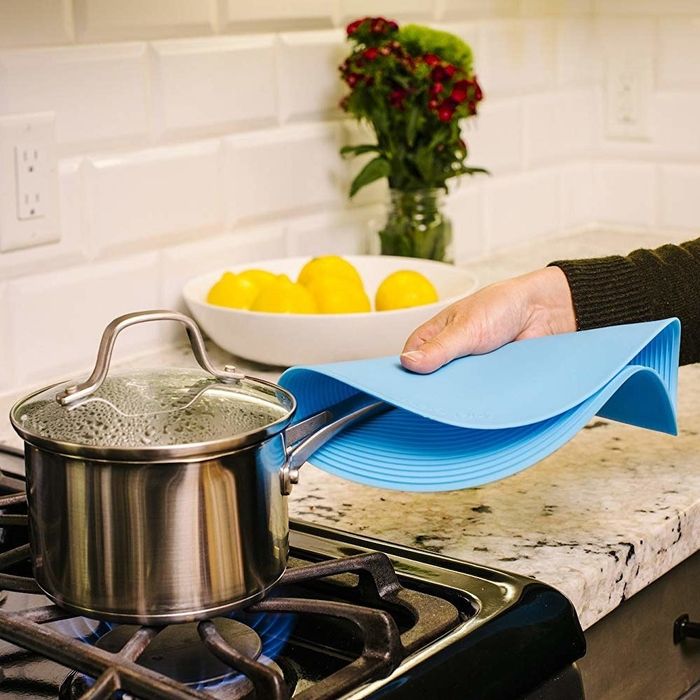 A hand lifting a pot off the stove using the large silicone round cover