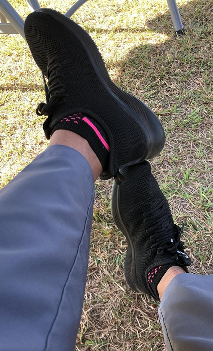 A close-up of a person's legs wearing gray pants and black knit sneakers