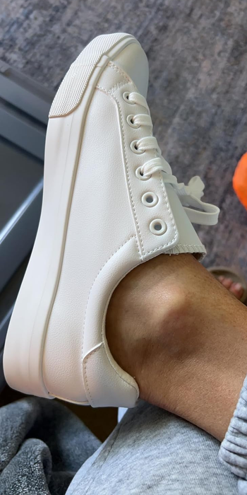 Someone wearing white, lace-up sneakers. The shoe is the focal point, showcasing its design and style