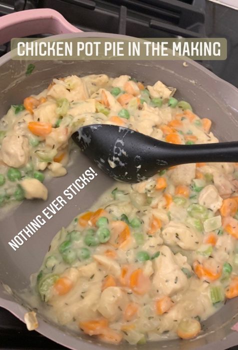 A pan filled with chicken pot pie filling, showcasing a clean stripe where the spoon scooped out the mixture, accompanied by a caption highlighting its nonstick feature: 'Chicken pot pie in the making—nothing ever sticks.'