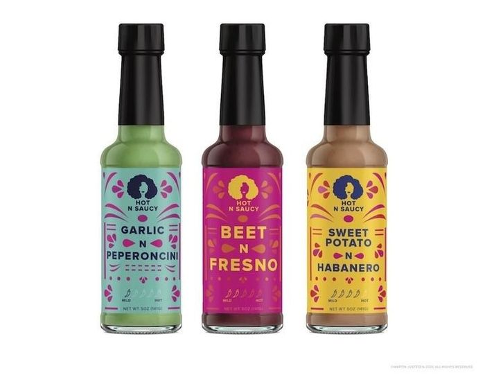 Three glass bottles of hot sauce in shades of red, orange, and green.