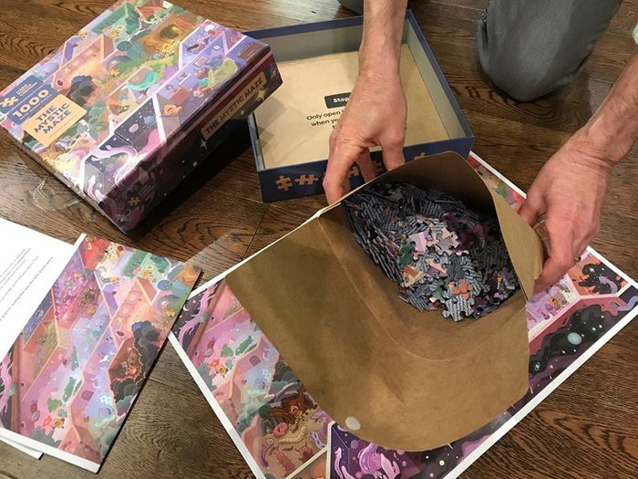 A paper bag filled with puzzle pieces next to the box displaying a maze scene featuring magical creatures