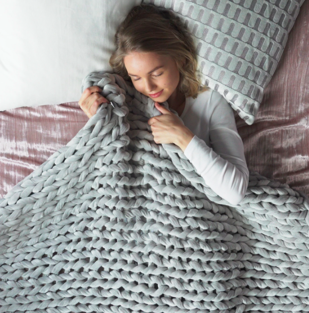 model snuggles under a large knitted blanket