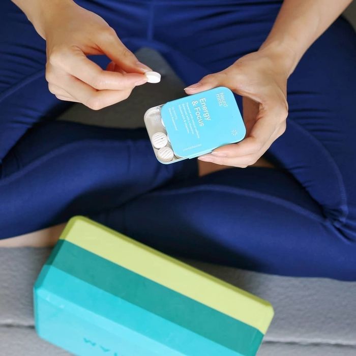 A model about to do yoga, holding a tin of mints in one hand and a single mint in the other hand