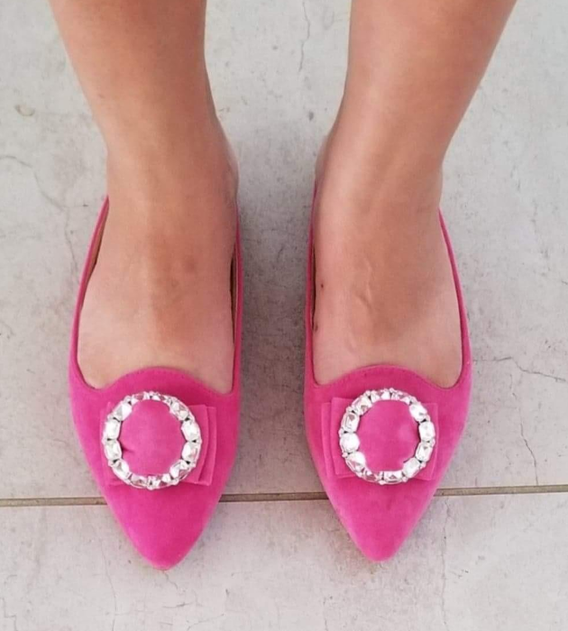 A reviewer sporting pointed-toe slip-on flats in pink suede-like fabric with a chic circular embellishment on top
