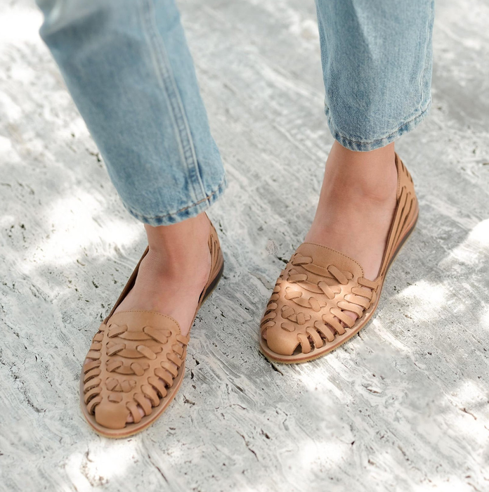 Person wearing light blue jeans and tan woven loafers standing on a textured white floor
