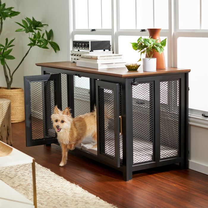 A black metal credenza with mesh wire and a front door, topped with wood, serving as a modern dog crate
