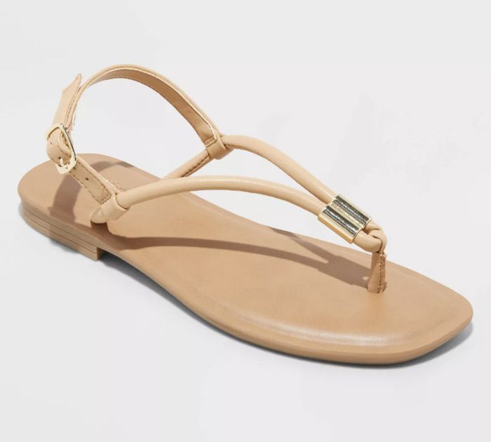 A single flat sandal with thin straps and a buckle, featuring a shiny metallic accent piece on the front