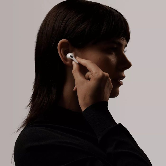 A side view of a model inserting an AirPod into their ear.