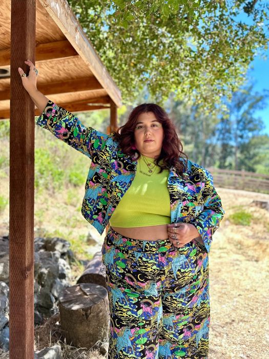 Model poses outdoors in vibrant, patterned pants and a coordinating jacket, topped off with a light green crop top, showcasing a bold, fashionable ensemble.