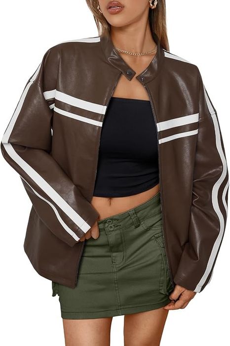 A woman models a chic, oversized leather jacket with white stripes, paired with a black tube top and green mini skirt.