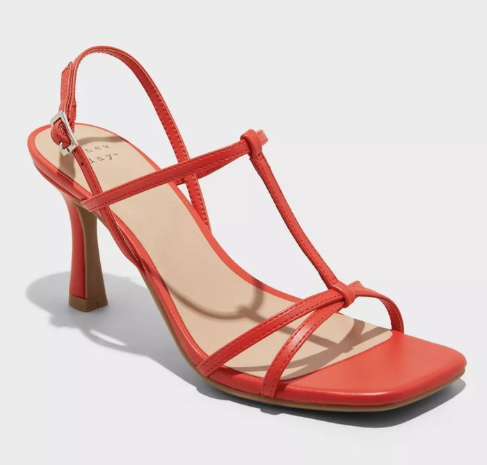 A red strappy high-heeled sandal with a slender heel. No one is shown in the image